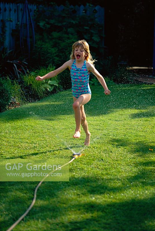 Young girl playing with a hosepipe in the garden