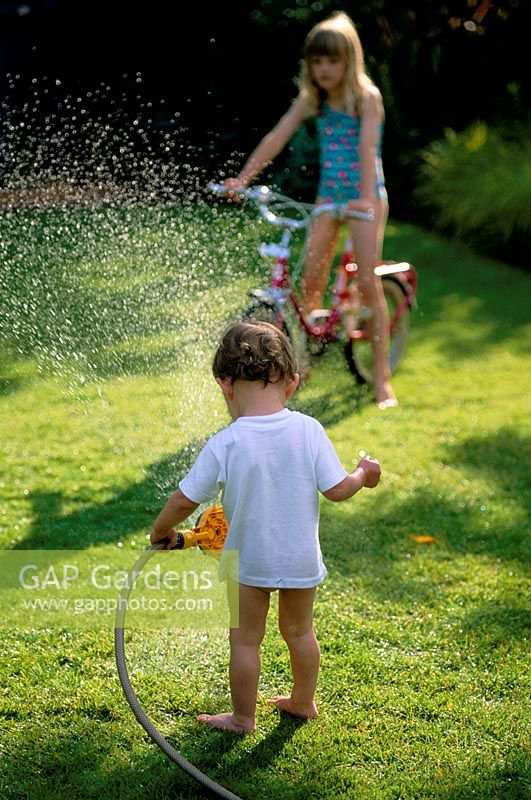 Children playing with a hosepipe in the garden