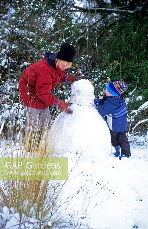 Mother and child making snowman in garden