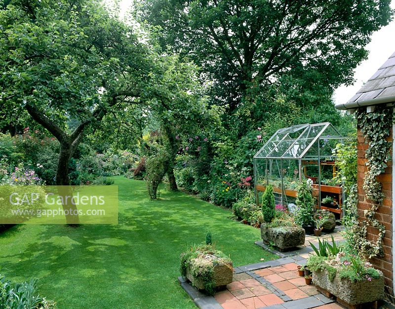 View down garden from back of house, with well-kept lawn and small greenhouse on left  