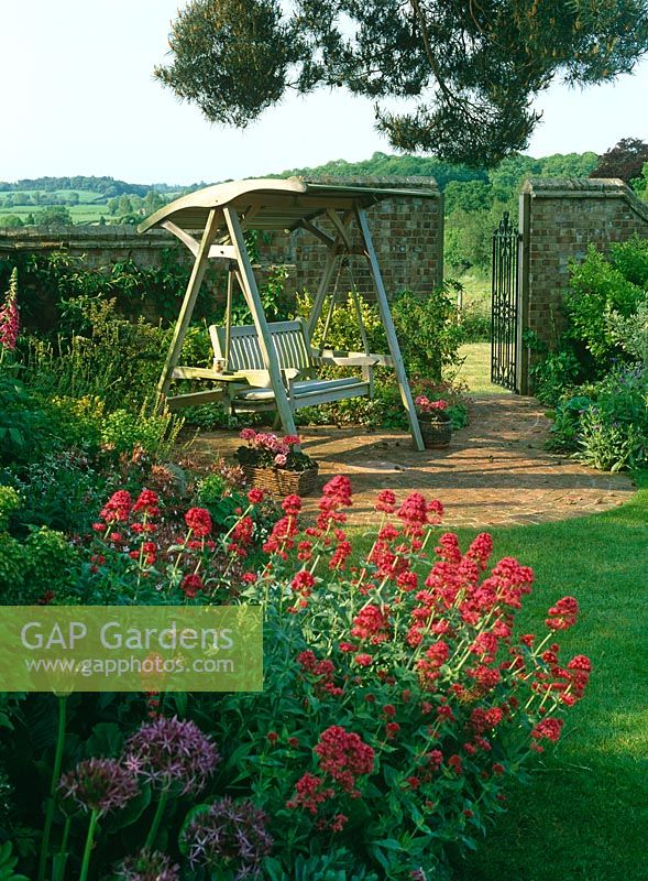 Centranthus ruber edging border by wooden swing seat with view to countryside beyond