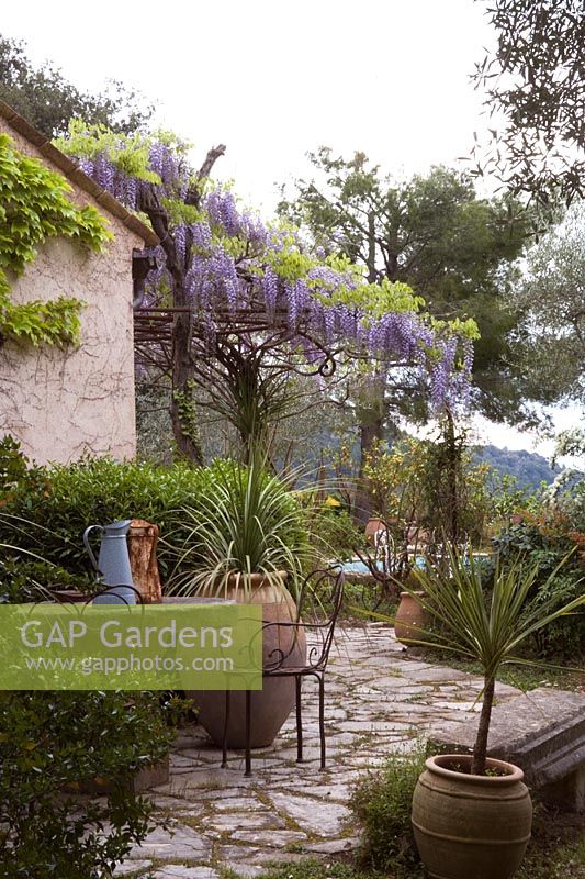 Outside eating area in Mediterranean garden with metal pergola with wisteria looking towards provencal hills