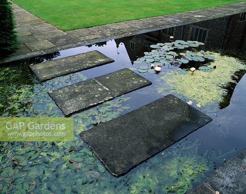 Stone slabs form a stepping stone bridge over a formal water garden planted with waterlilies