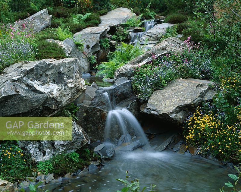 Waterfall over slate boulders with meadow planting