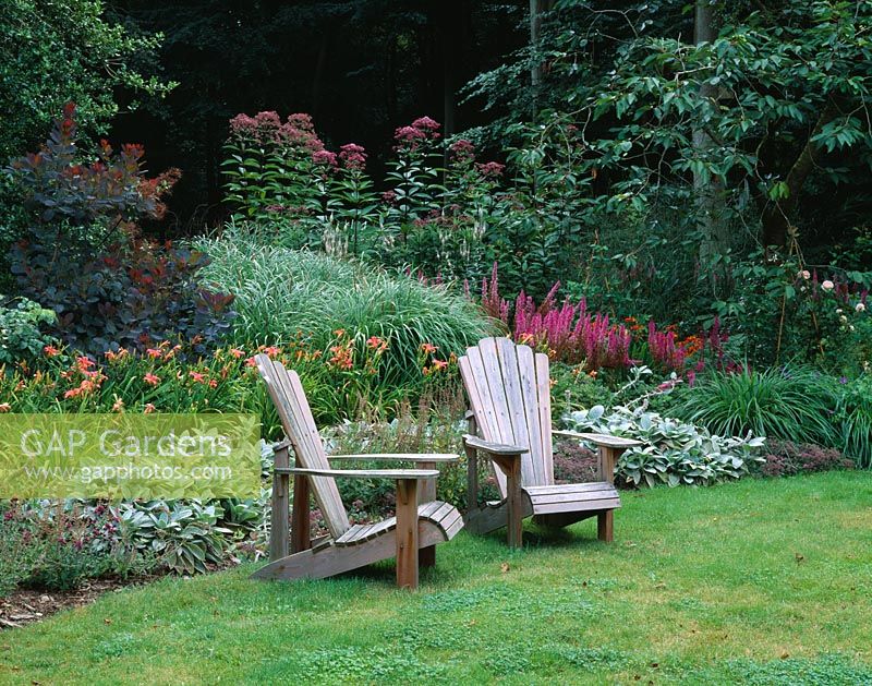 Two adirondack chairs in front of a border with Liatris, Hemerocallis and Eupatorium