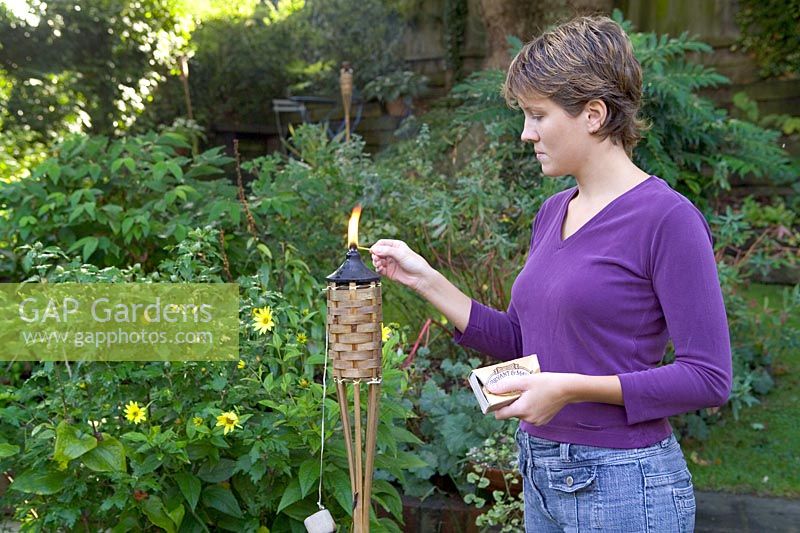 Lady lighting a garden flare with matches, evening light