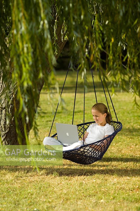 Teenage girl sitting in hanging chair with laptop