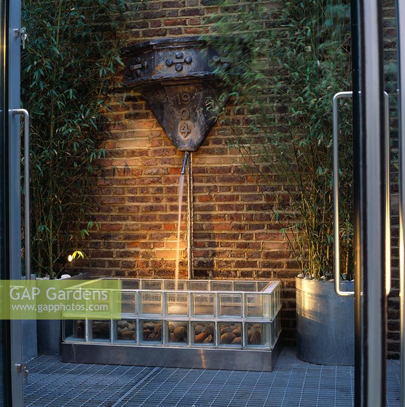 Water feature - water spout cascades onto sea-worn pebbles in fountain base of  transparent glass bricks in designer Stephen Woodhams' own garden