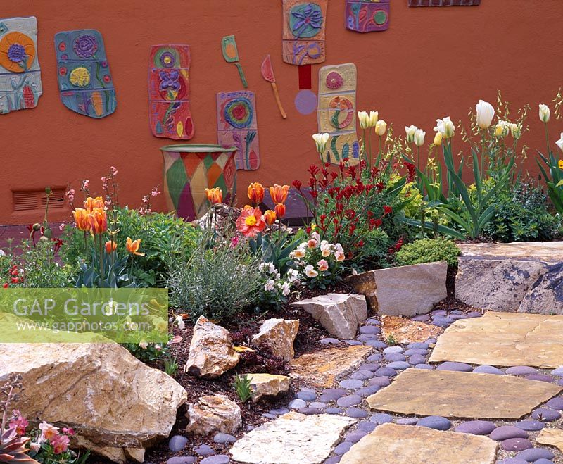 Coloured wall with ceramic pictures. In foreground are Tulipa and arizona flag stone and mexican cobbles - California