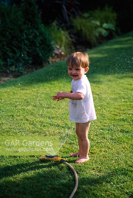 Toddler playing with a hosepipe in the garden.
