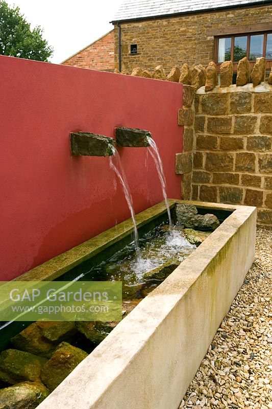 Water feature with water spouts in red wall and trough 