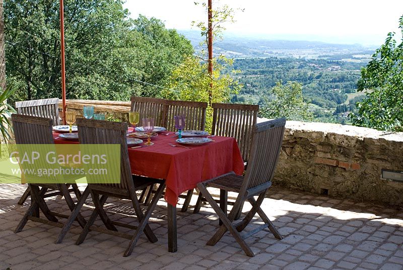 Stone terrace in old Tuscan farmhouse with wooden table and chairs and sun canopy - View to Tuscan landscape in Italy