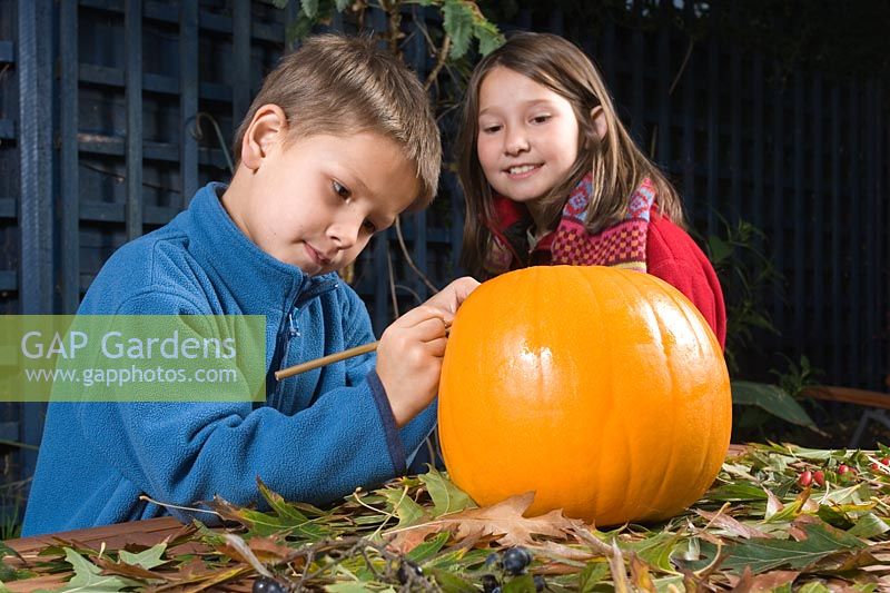 Young boy drawing a face on pumpkin