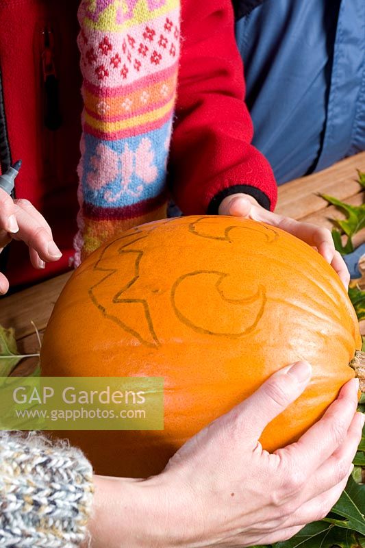 Girls drawing a face on pumpkin, sequence of making Halloween lantern