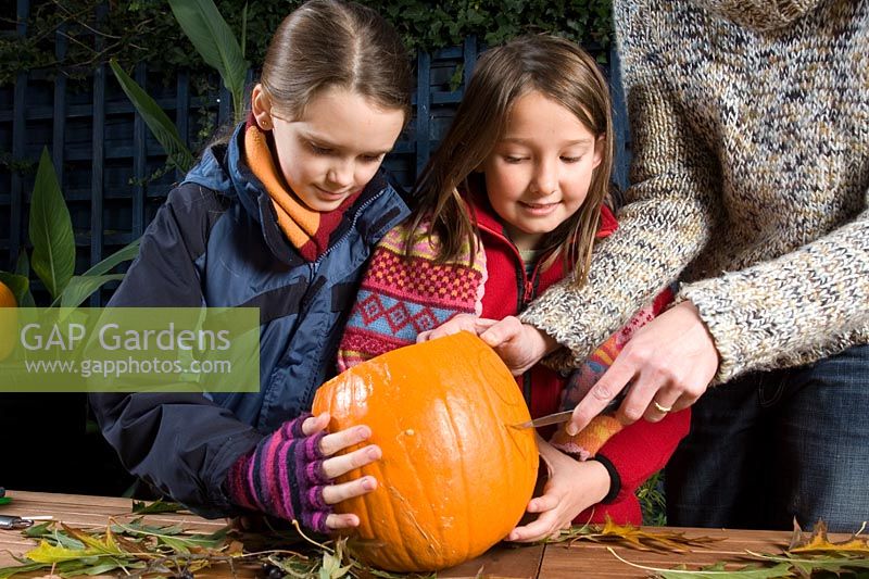 Girls watching while adult cuts face with sharp knife in pumpkin, sequence of making Halloween lantern