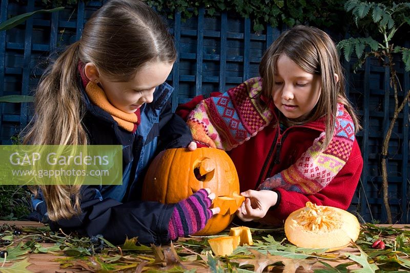 Girls removing mouth cut with sharp knife in pumpkin, sequence of making Halloween lantern