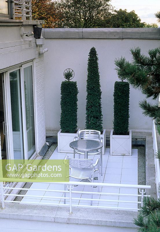 Contemporary stylish urban roof garden with metal table and chairs and topiary in containers - London  