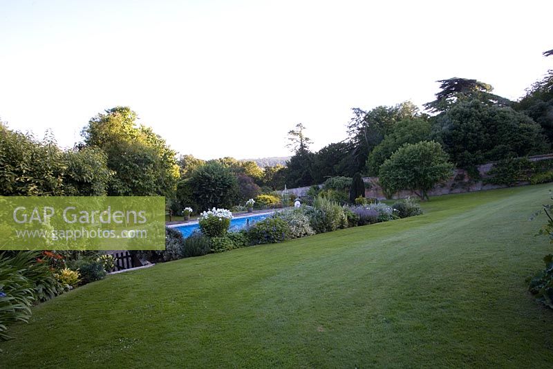 Swimming pool enclosed within walled garden and surrounded by borders. Softening of modern leisure feature through perennial planting.