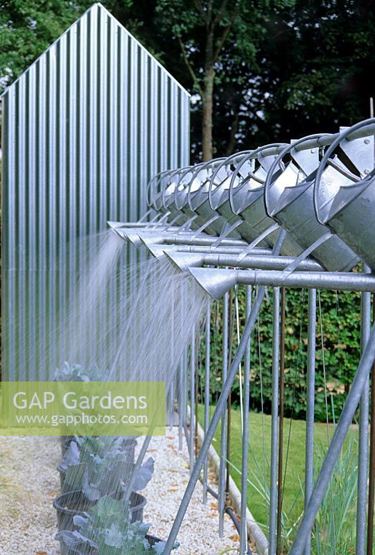 Line of suspended metal watering cans angled to water pots with vegetables at  Chaumont, France. 