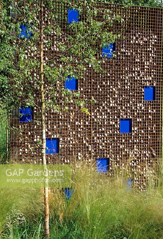 Dividing wall of gabions filled with pebbles punctuated with blue glass plates - Westonbirt Garden Festival  
