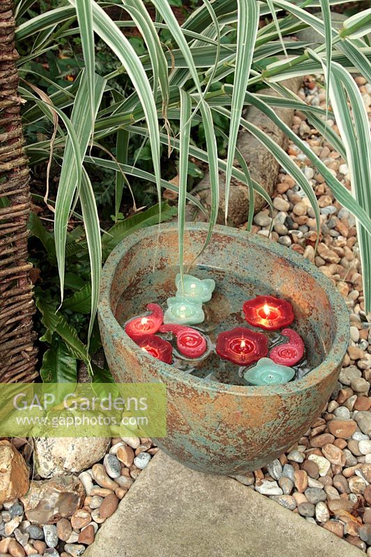 Red and green candles floating in a large decorative oval bowl in garden with Arundo donax var. versicolor