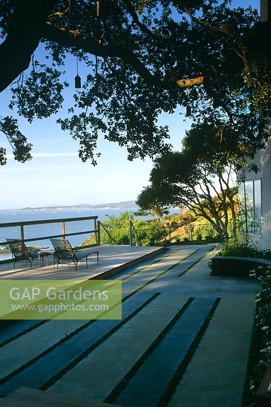 Contemporary concrete patio overlooking ocean. Parrallel lines planted with green plants - CA USA