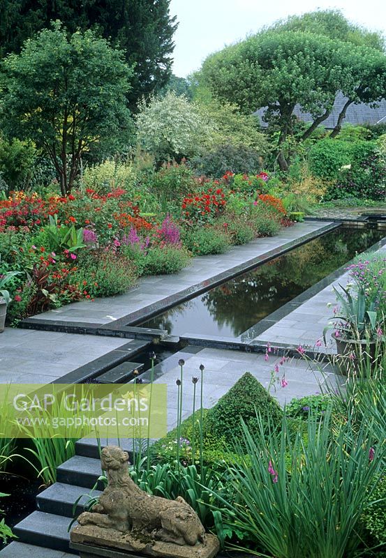 Formal town garden with long rectangular water rill and hot coloured border. Stone path and steps with lion ornament - Dublin, Republic of Ireland
