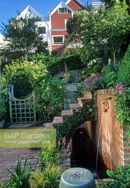 Small urban garden with raised bed and steps over water feature with spout. Arch with climber over gate - San Francisco USA 