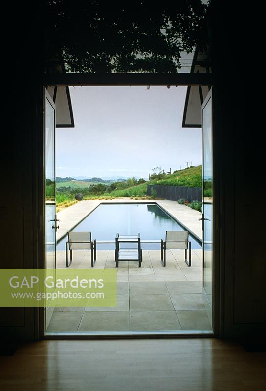 View from inside to elongated swimming pool with table and two chairs. Landscape in background - The Tambor Vineyard, Napa Valley, California USA