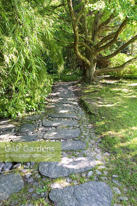 Path made from large stone slabs and cobblestones leading through Japanese garden - The Gardens at Norrviken