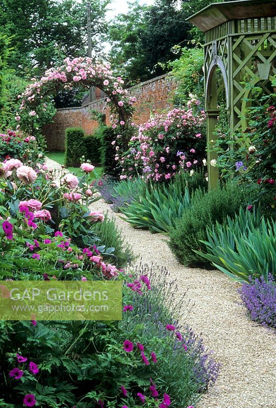 Walled garden with mixed borders of Paeonia, Lavandula, Iris and Geranium. Rosa arch and wooden gazebo - Seend Manor, Wiltshire 