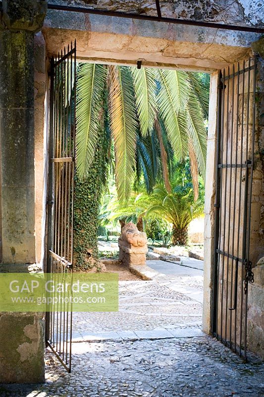Doorway leading to Jardines de Alfabia, Mallorca with palm trees and stone lion statue, cobble stone floor