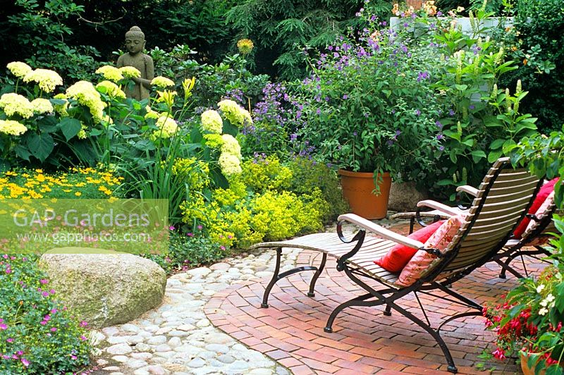 Two reclining chairs facing a mixed border with Hydrangea, Alchemilla mollis and a Buddah statue
