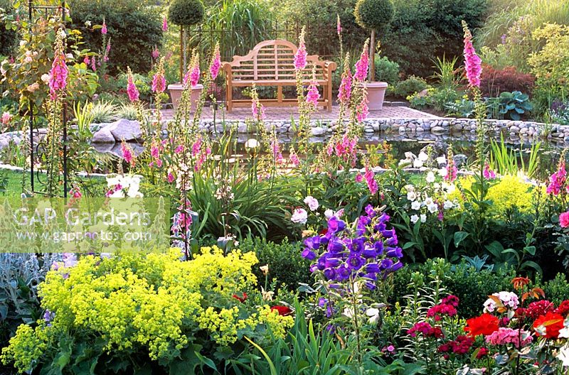 Cottage style garden with seating area and pond in backgound