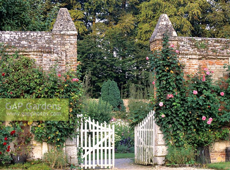 Garden entrance with high brick wall and painted white gates