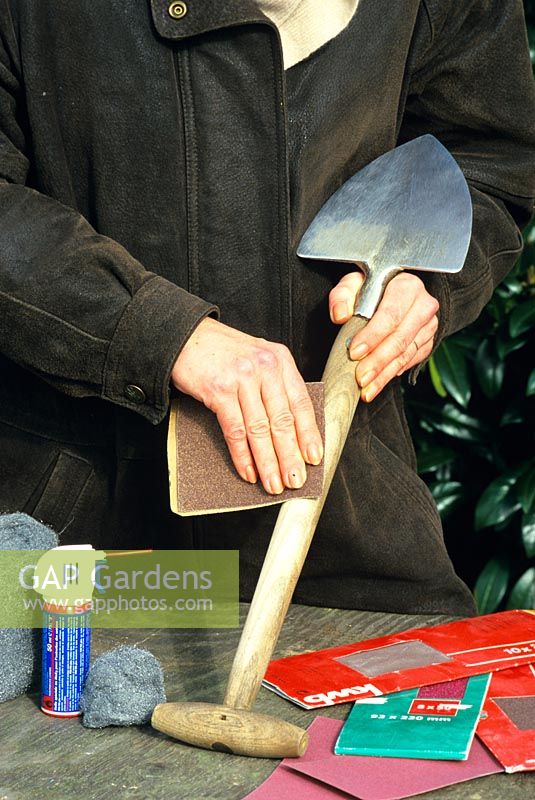 Woman cleaning wooden handle of spade with sandpaper