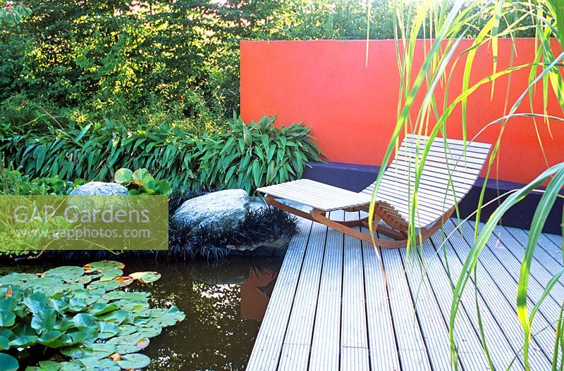 A reclining chair with water and decking in a contemporary garden