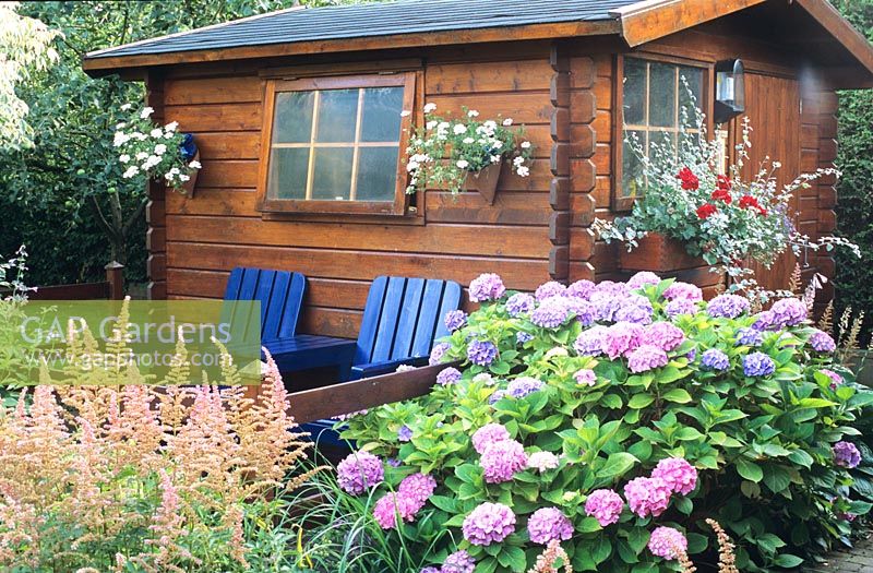 Two seats in front of log cabin decorated with hanging plants