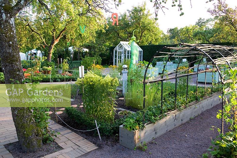 Rustic pergola with sweetpeas and vegetable garden in background - Apple tree above with letters from the alphabet hanging, small green house in background, Maja's garden for children, Sofiero Castle, Sweden 