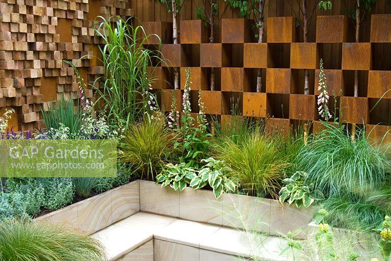 Mixed grasses and perennials surround a sunken seating area with a backdrop of walls created from corten steel boxes and irregular wooden blocks - Garden - The Pemberton Greenish Recess Garden, Designer - Paul Hensey with Knoll Gardens, Sponsor - Pemberton Greenish