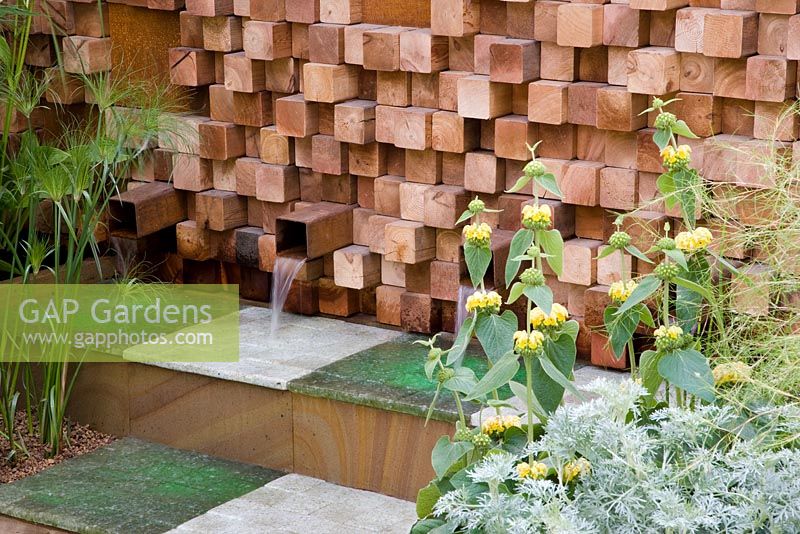 Wooden block wall with water spouts. Plants include Artemisia 'Powis Castle', Phlomis russeliana and Cyperus papyrus. The Pemberton Greenish Recess Garden, Design - Paul Hensey