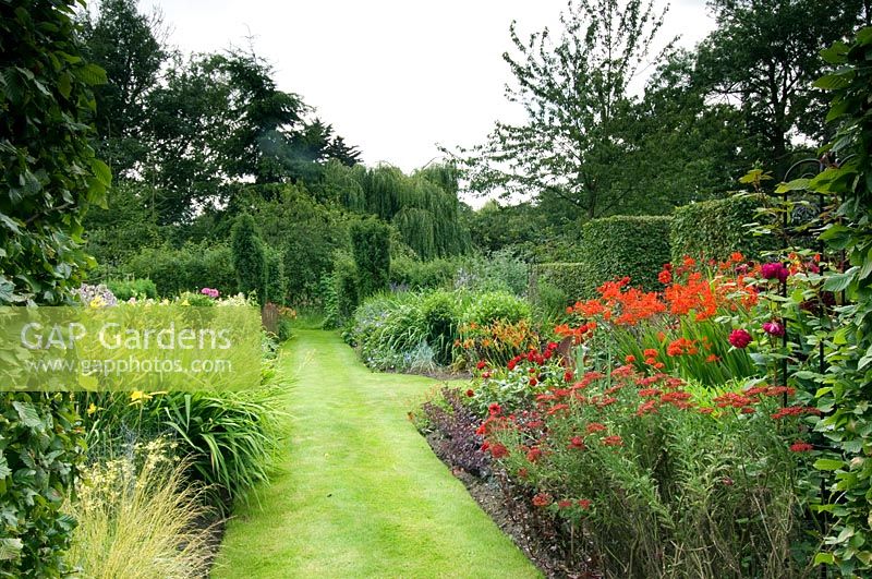 Summer garden with grass path and hot coloured border of Dahlias, Roses, Crocosmia and Achillea - Devils End Haddiscoe, Norfolk