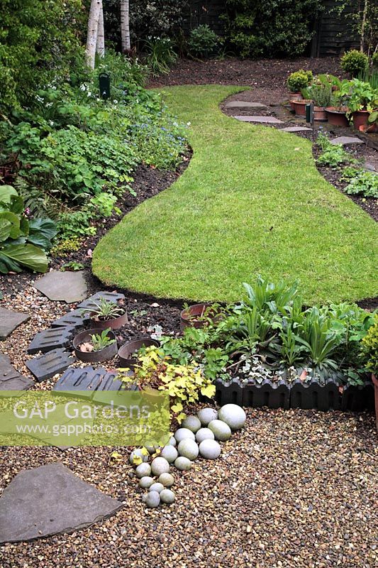 Simple ovoid shaped lawn in well tended garden in spring with Victorian tiles as decoration