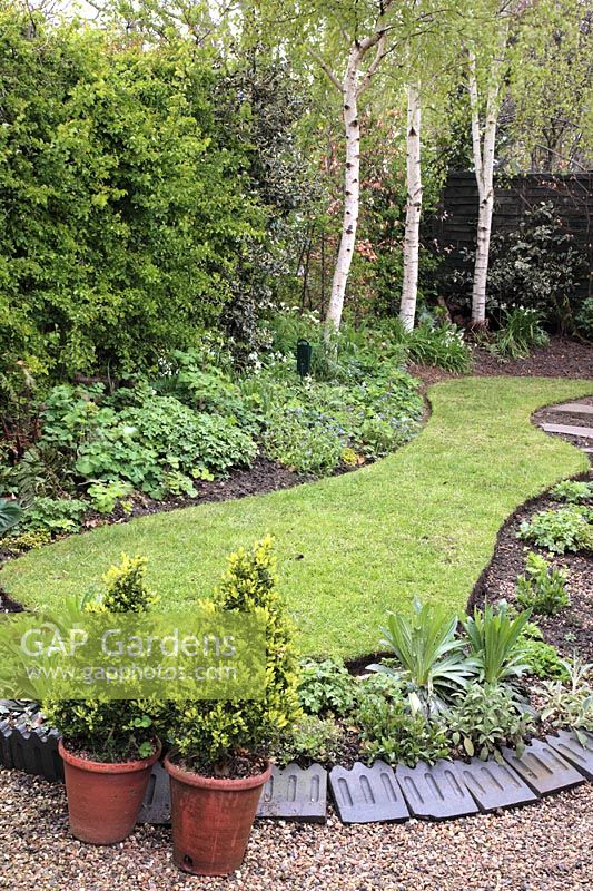 Simple ovoid shaped lawn in well tended garden in Spring with Victorian tiles as decoration