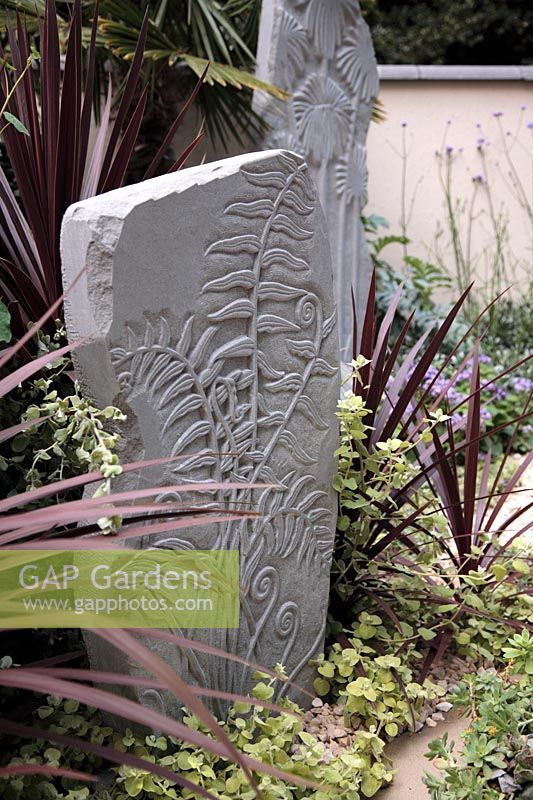 Cordyline australis 'Atropurpurea' and   Helichrysum petiolare 'Lime Light' beside  sandstone monoliths with fern design - 
Garden - The Way Forward, Designers - Zoe Cain, with Jim Buttress VMH and Jocelyn Armitage, for St. Joseph's Hospice and Perennial Gardeners' Royal Benevolent Fund
