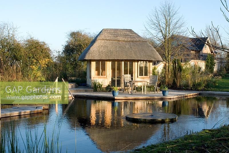 Natural swimming with thatched timber pool house surrounded by decking in November