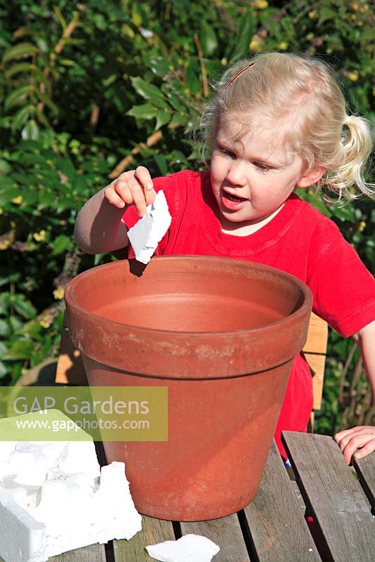 Young child girl putting polystyrene pieces in terracotta pot for drainage
