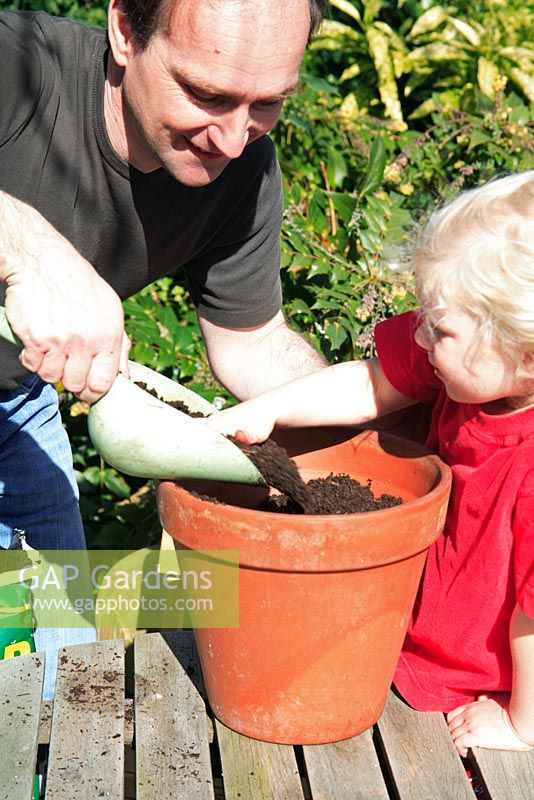 Young child girl and man putting compost in terracotta pot 