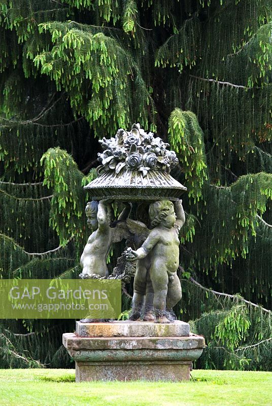 Stone statue of cherubs with weeping conifer in the Temple Garden, Cholmondeley Castle, Cheshire 