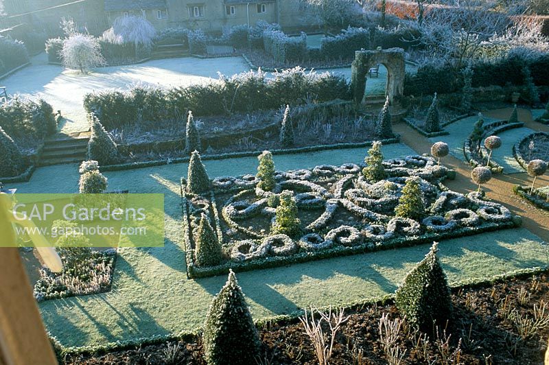 View across the frosted celtic knot garden with lollipop topiary and the Saxon arch - The Abbey House, Wiltshire